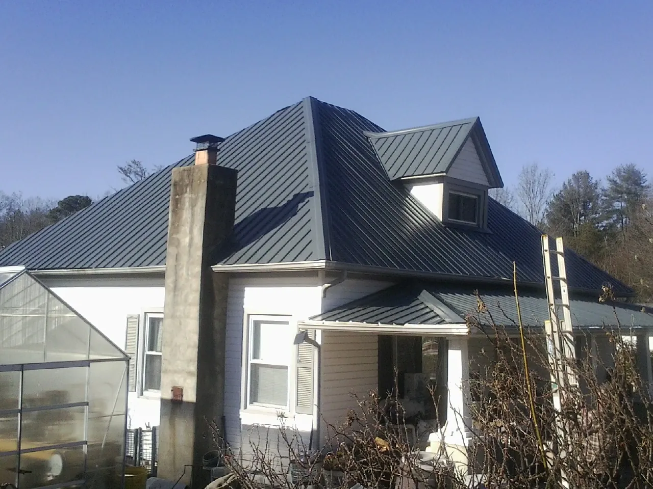 Dark blue standing seam metal roof on a white farmhouse with dormer — Slate & Tile Roof Repair by Roofing Brothers in Deadwood