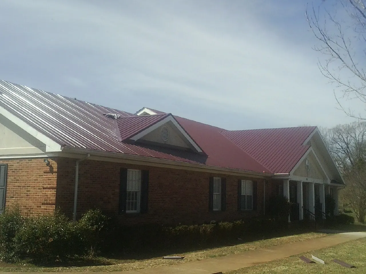 Red metal roof with gabled entries on a long brick building, from a Hail Damage Roof Repair job in Deadwood
