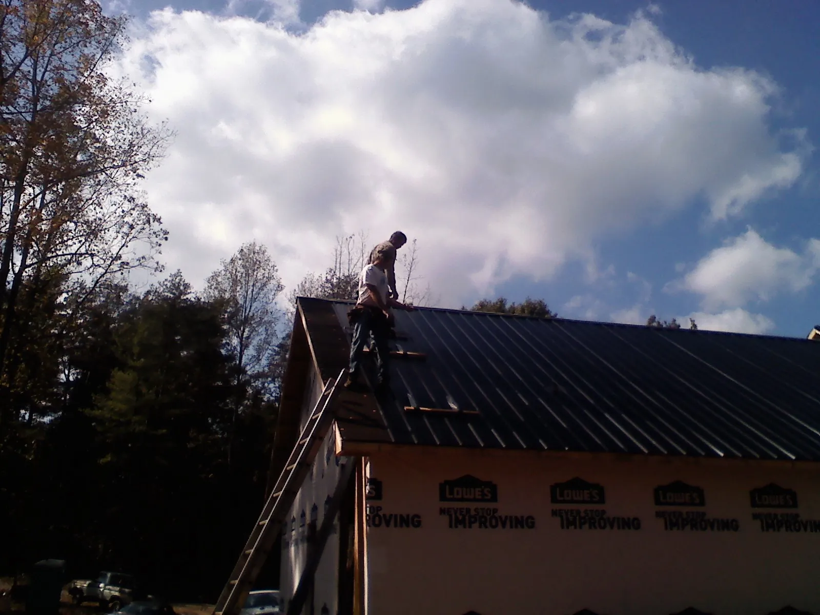 Roofer fastening dark metal panels high against a cloudy sky, from a Roof Inspection job in Deadwood